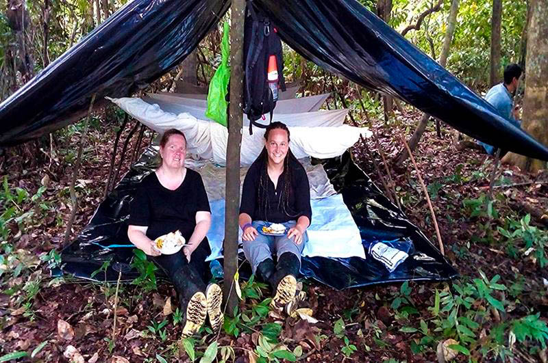 Two tourists enjoying lunch in the middle of the rainforest at Pacaya Samiria Reserve, surrounded by lush Amazon jungle, experiencing authentic eco-tourism in Peru.