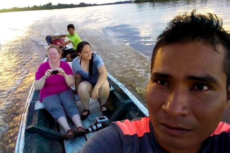 Four people are riding in a small boat on a river at sunset_ a man takes a selfie while two women and a boy enjoy the ride and the scenic view