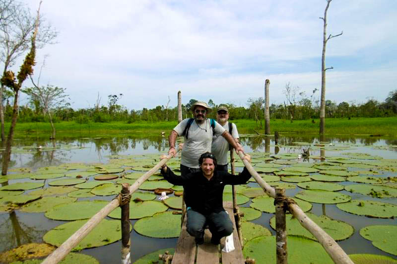 Tourists posing in front of giant Victoria Amazonica water lilies, smiling and surrounded by lush tropical vegetation