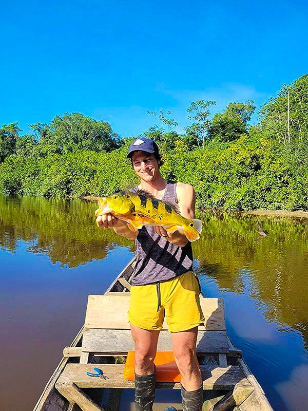 Tourist fisherman holding a freshly caught peacock bass fish in Pampa Caño stream, surrounded by lush Amazon rainforest, enjoying sport fishing and eco-tourism in the Peruvian Amazon.